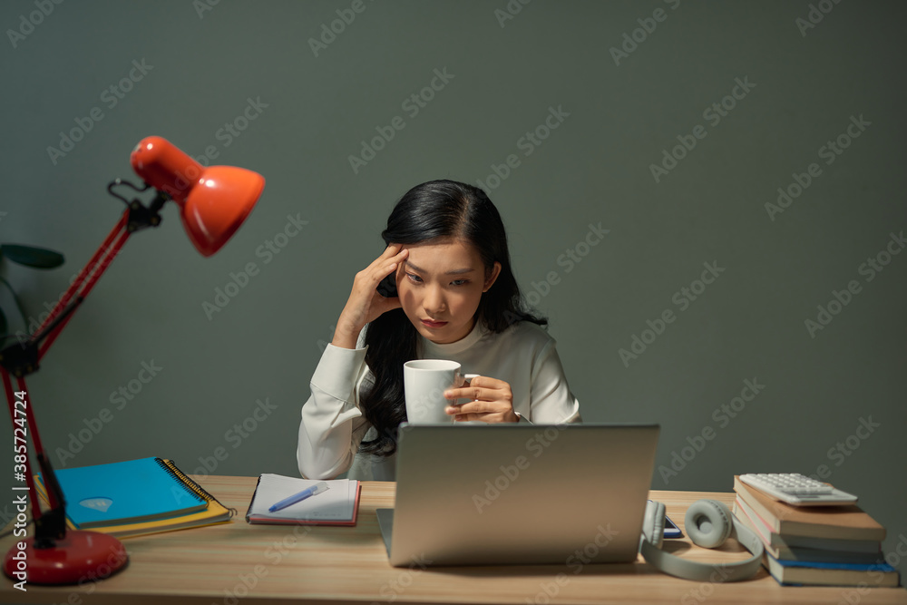 Pretty young student sitting at desk and doing her homework, she is connecting to the internet with 