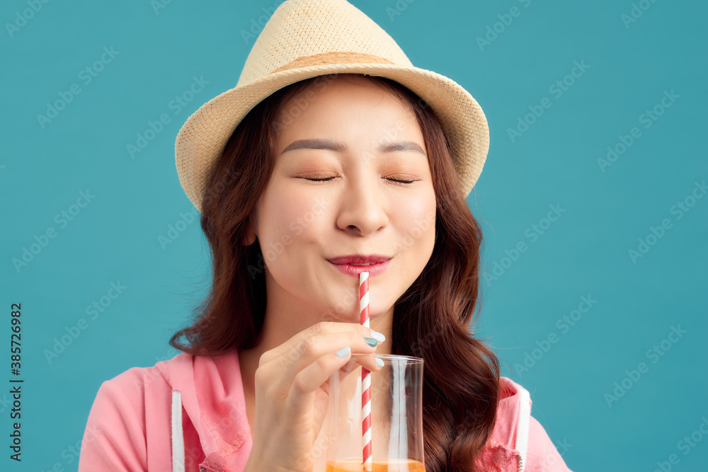 Cheerful you Asian woman drinking fruit juice and wearing straw hat, white t-shirt, short jeans, pin