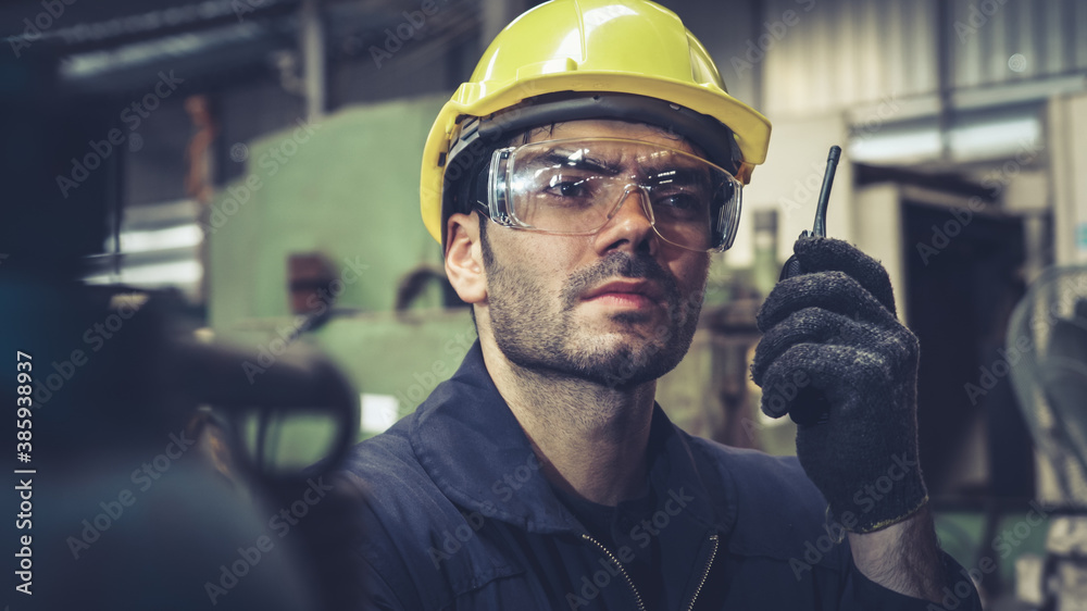 Factory worker talking on portable radio while inspecting machinery parts . Industrial and engineeri