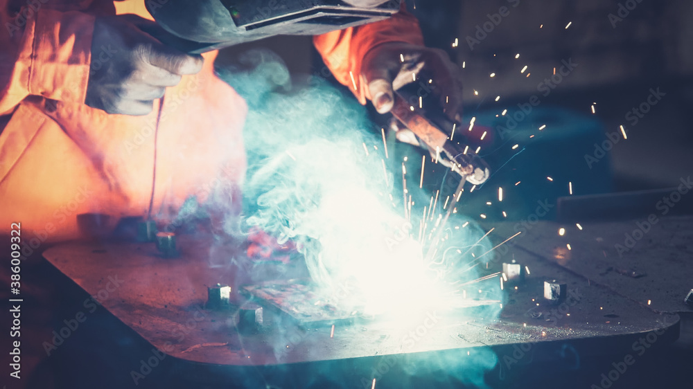 Metal welder working with arc welding machine to weld steel at factory while wearing safety equipmen