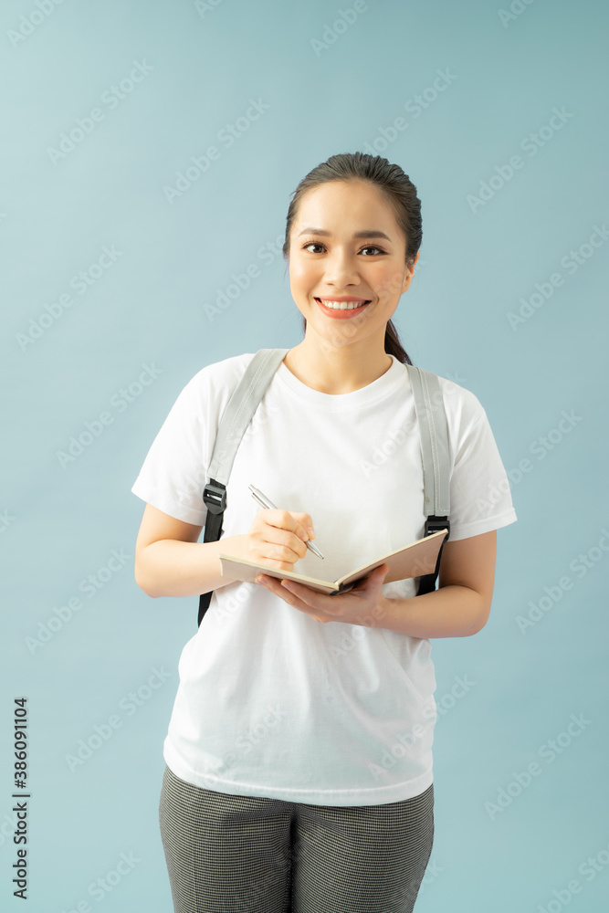 Portrait of a happy friendly girl student with backpack holding books  isolated over blue background