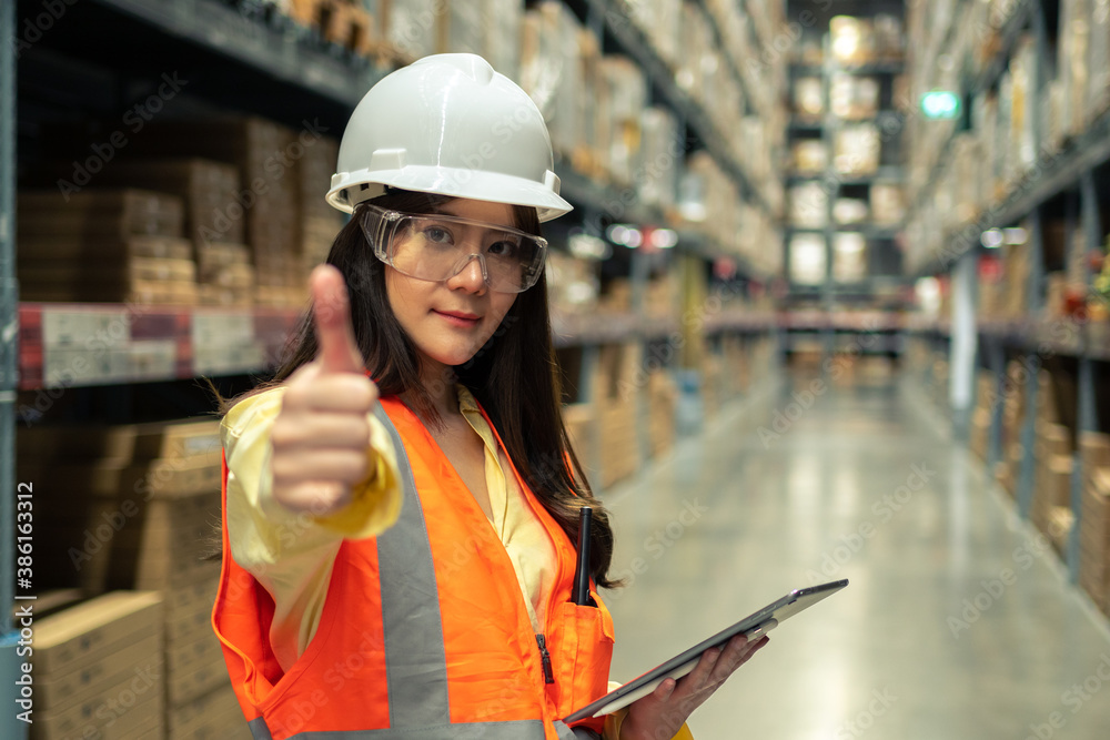 Female warehouse worker inspecting a warehouse in a factory. Wear a safety helmet and glasses for wo