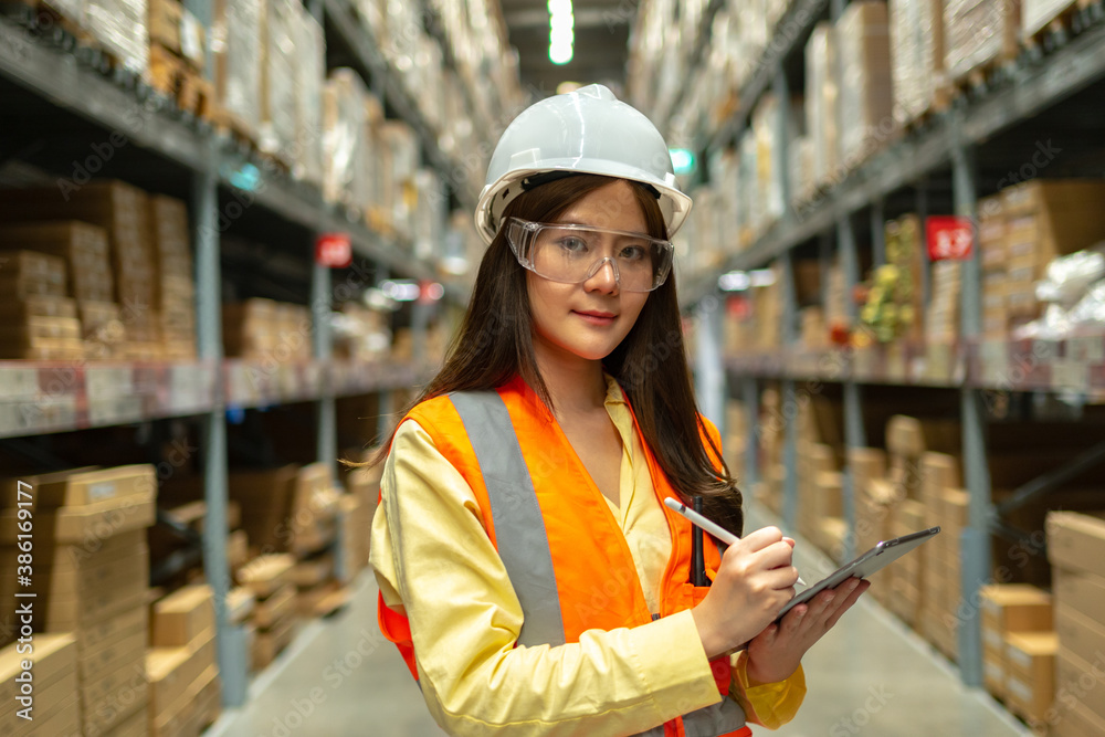 Female warehouse worker inspecting a warehouse in a factory. Wear a safety helmet and glasses for wo