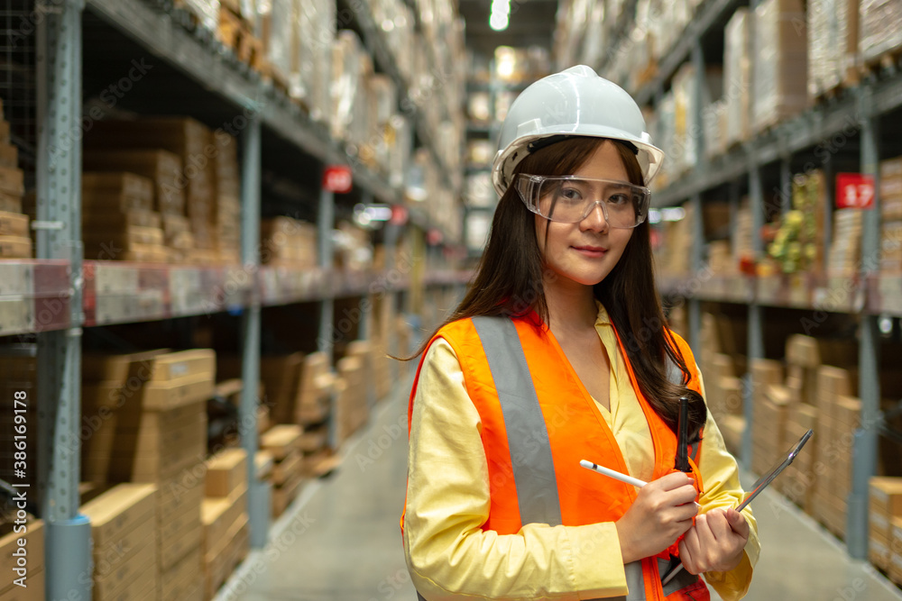 Female warehouse worker inspecting a warehouse in a factory. Wear a safety helmet and glasses for wo