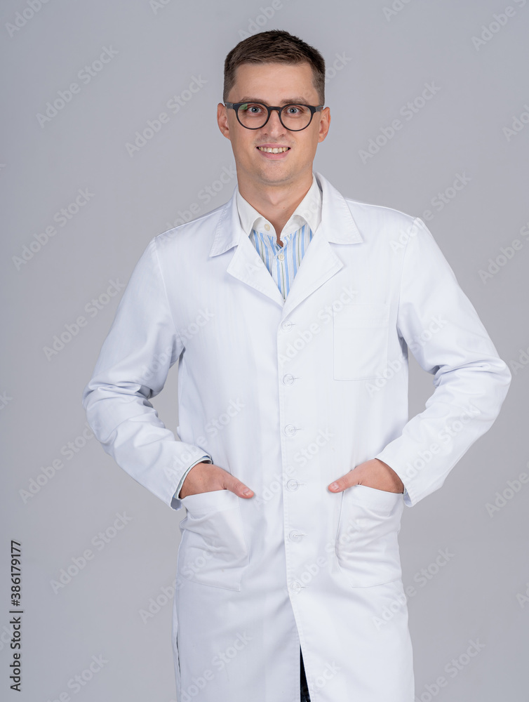 Studio portrait of a doctor or medical specialist. Standing with hands in pockets. Man in scrubs. Gr