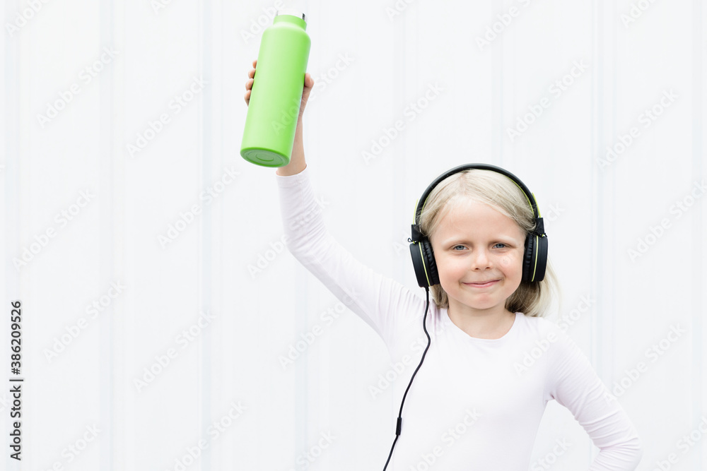 Young blond girl on white background drink fresh spring water from green reusable bottle. Healthy li