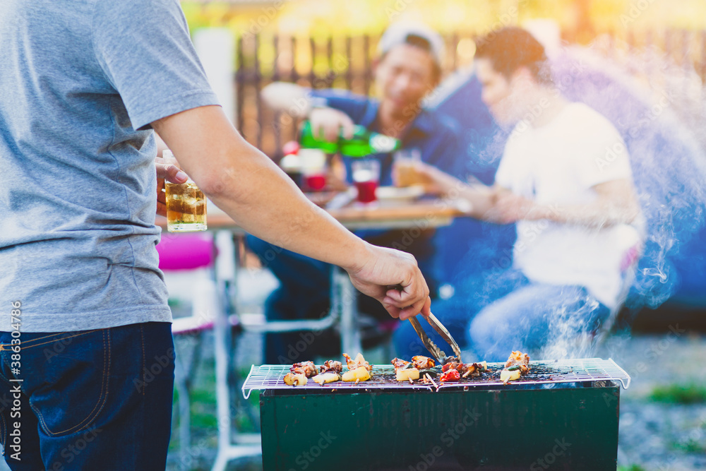 A young man grills a barbecue steak on a charcoal grill at an outdoor party with friends at home.