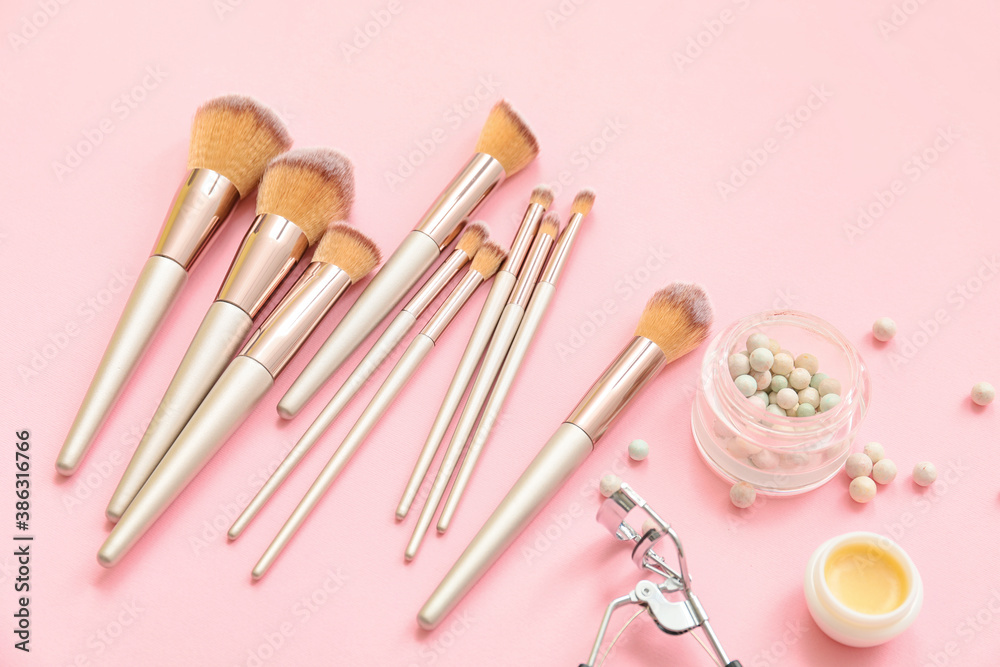 Set of makeup brushes with cosmetics on color background