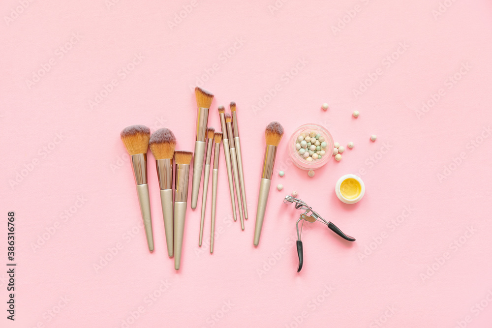 Set of makeup brushes with cosmetics on color background