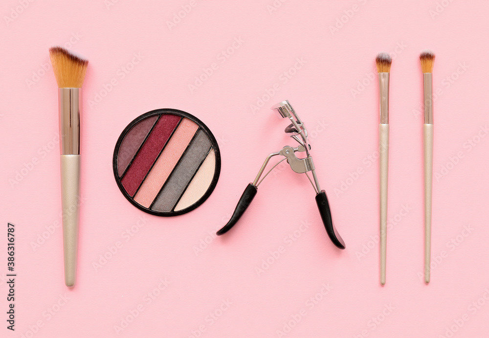 Set of makeup brushes with eyelash curler and eyeshadows on color background