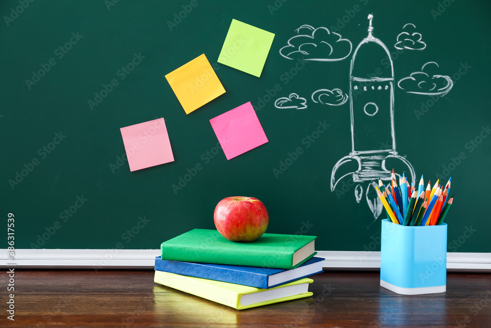 Books and stationery near chalkboard in classroom