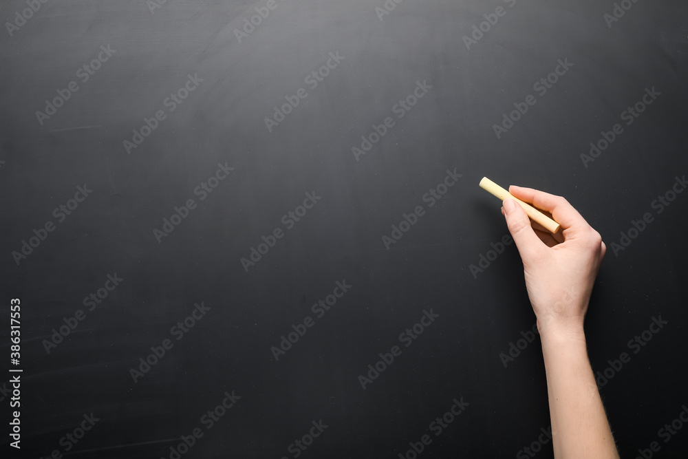 Female hand with piece of chalk on blackboard