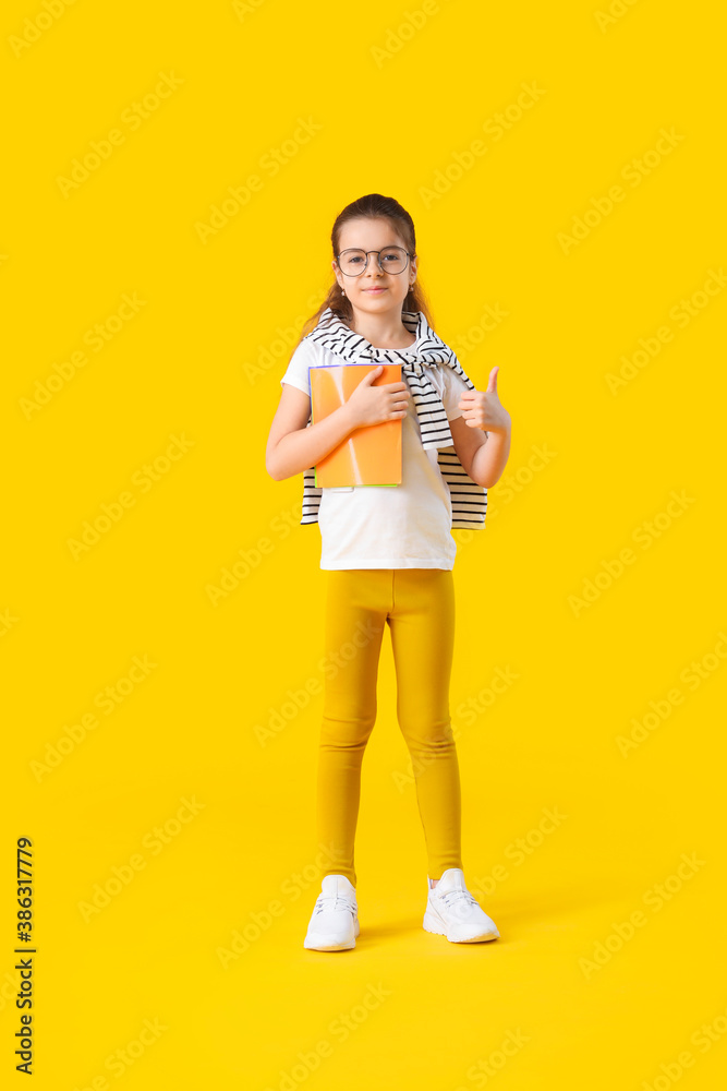 Cute little schoolgirl showing thumb-up gesture on color background