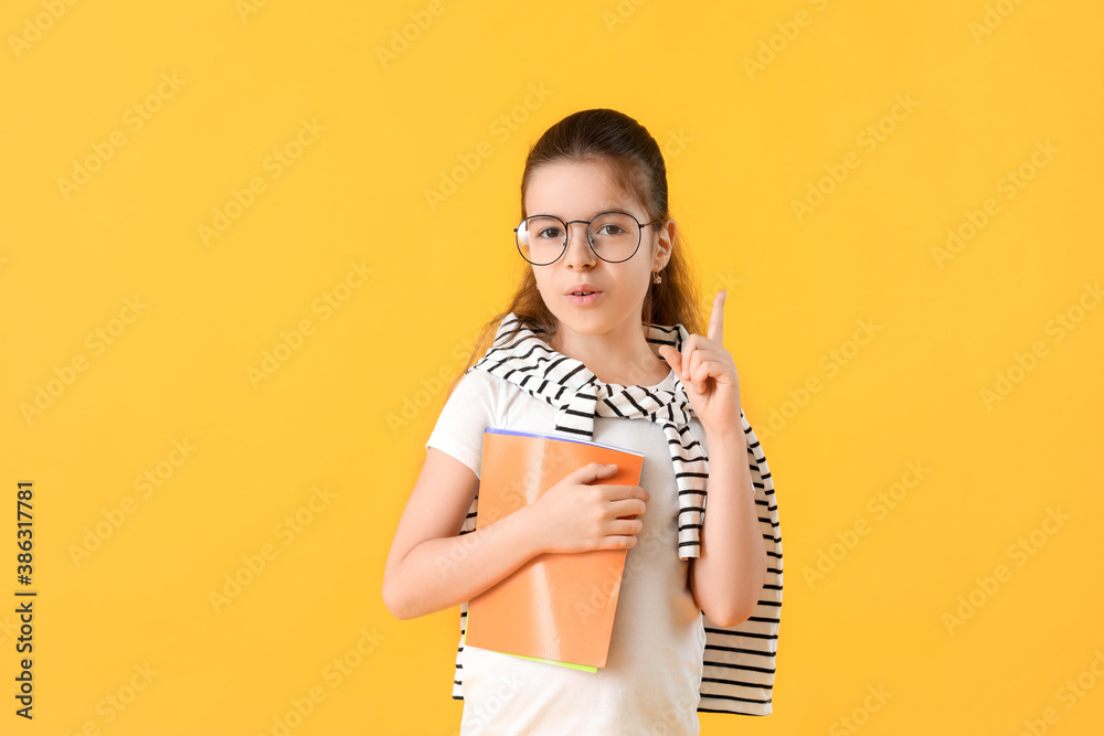 Cute little schoolgirl with raised index finger on color background