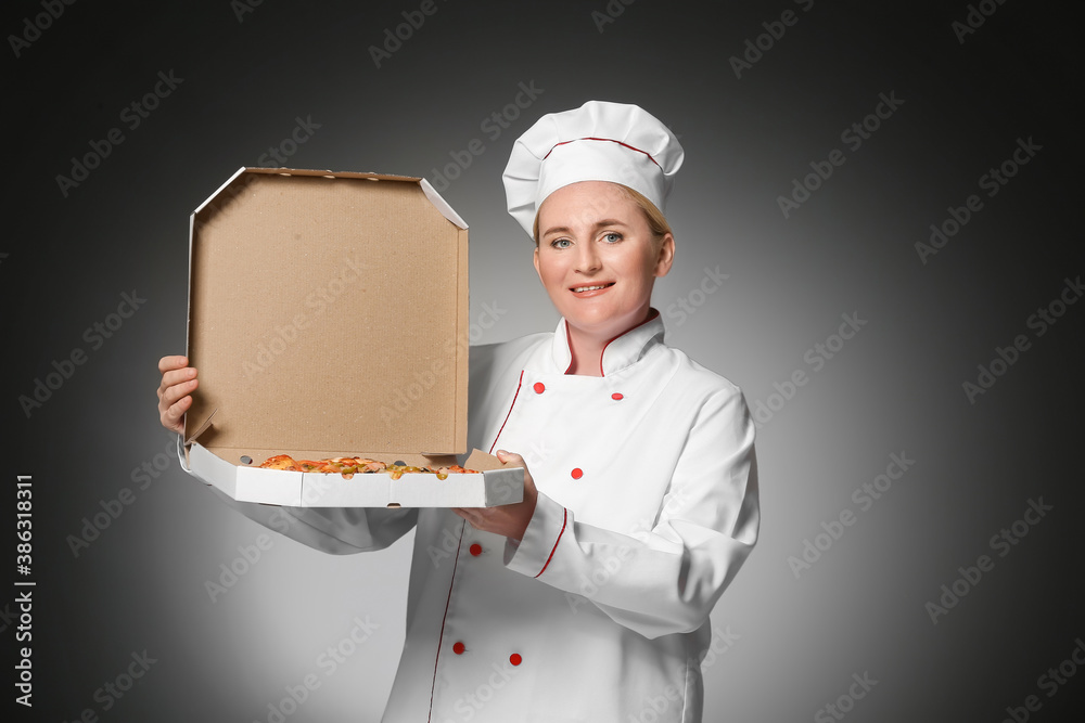 Mature female chef with tasty pizza on dark background