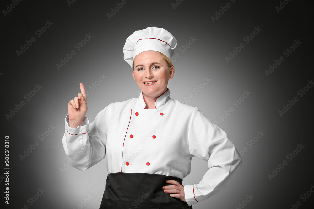 Mature female chef pointing at something on dark background