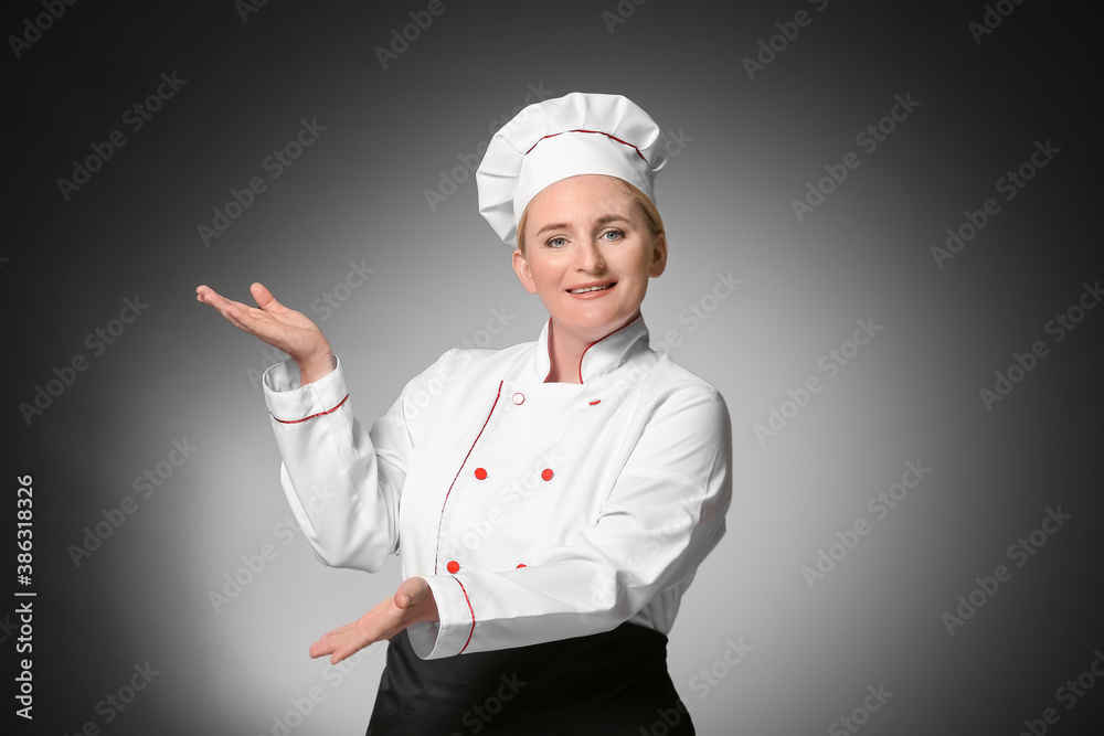 Mature female chef showing something on dark background