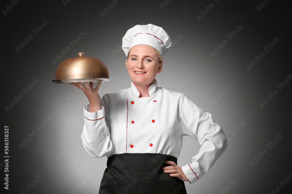 Mature female chef with tray and cloche on dark background