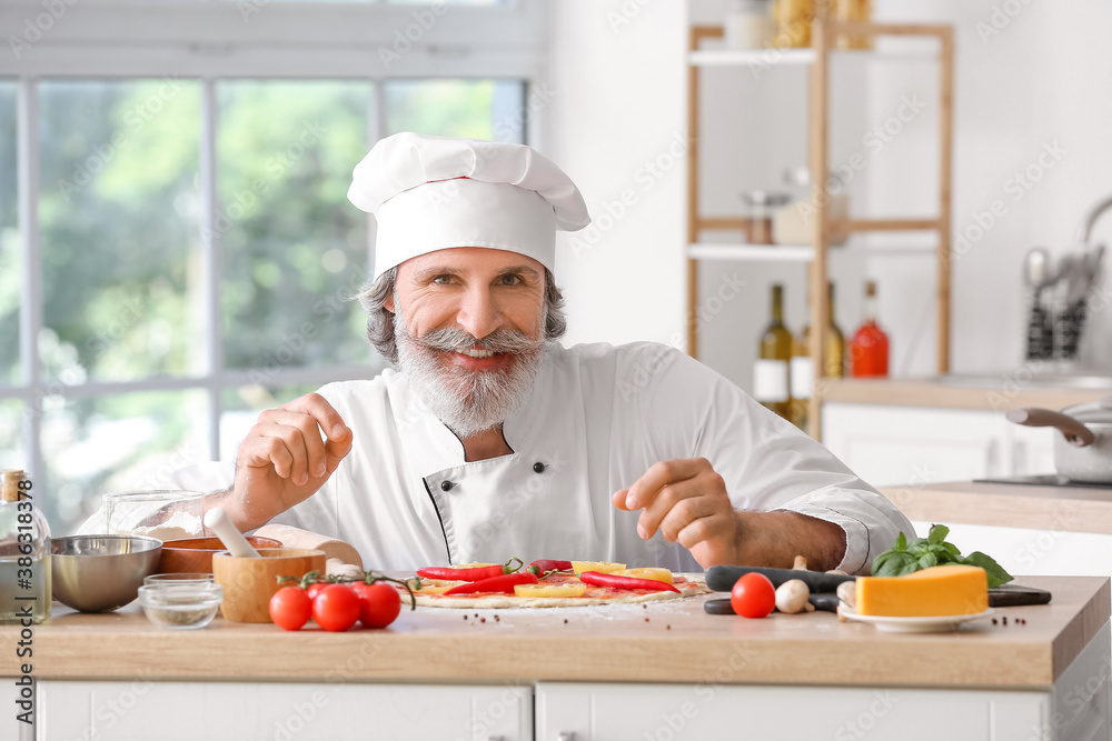 Mature male chef cooking tasty pizza in kitchen