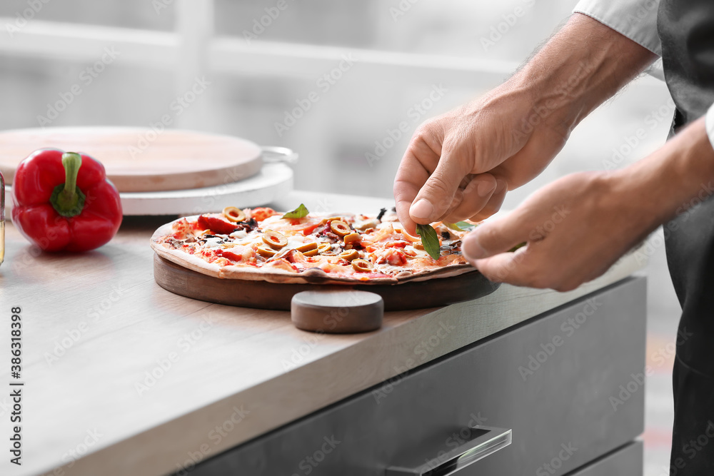 Mature male chef cooking tasty pizza in kitchen, closeup