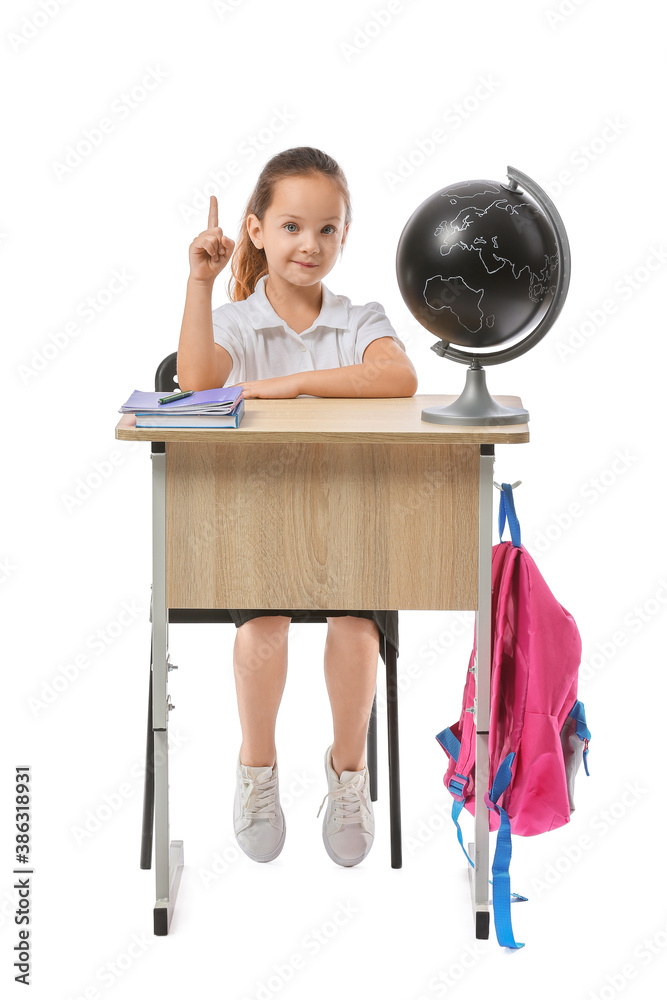 Little pupil with raised index finger sitting at school desk against white background