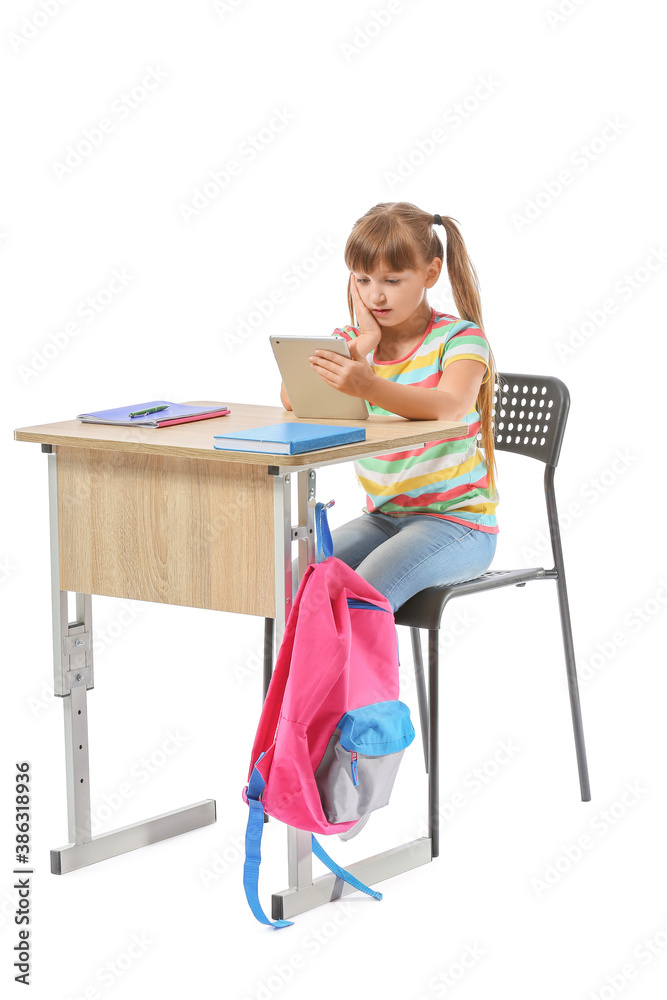 Little pupil with tablet computer sitting at school desk against white background