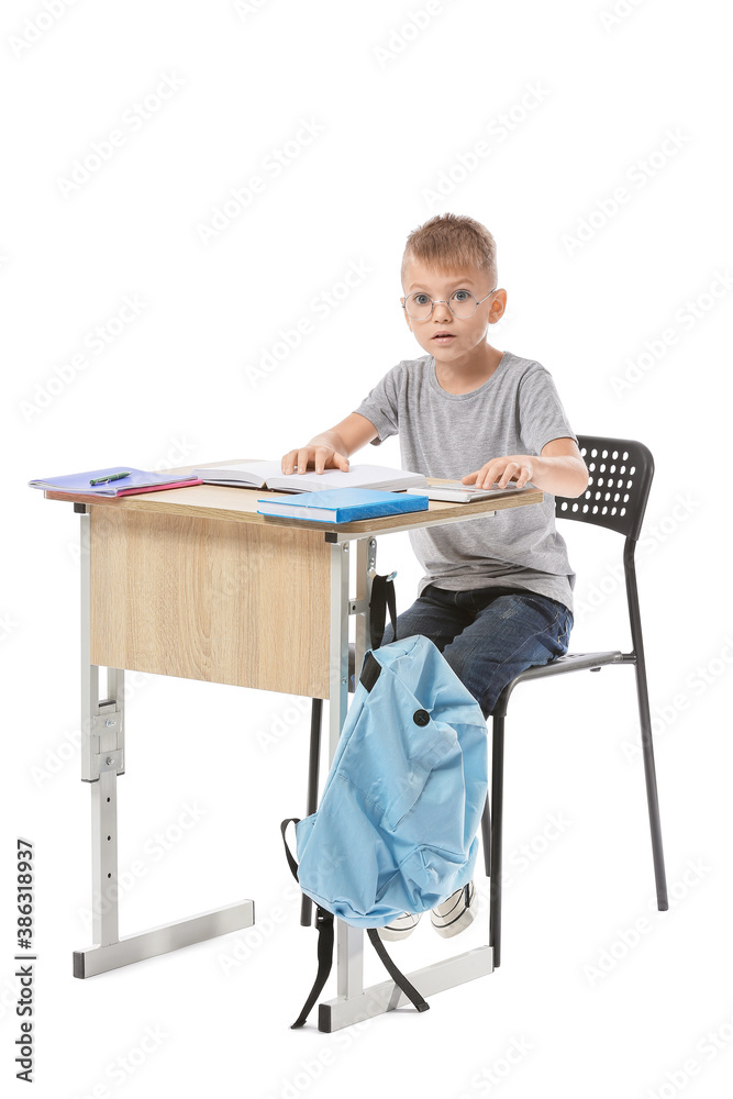 Little pupil sitting at school desk against white background