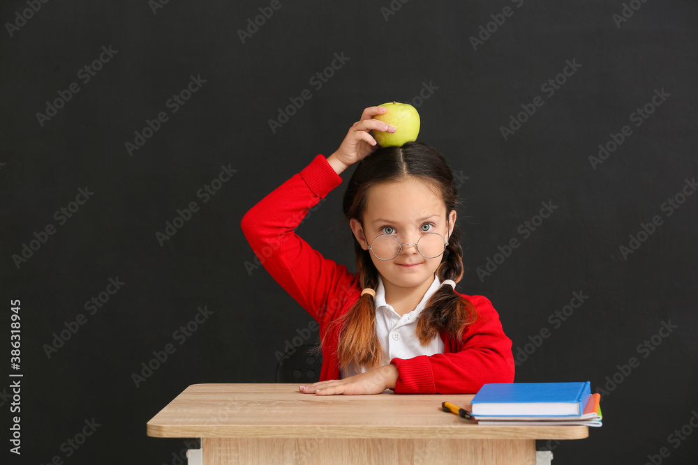 Little pupil sitting at school desk against dark background