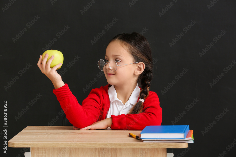 Little pupil sitting at school desk against dark background