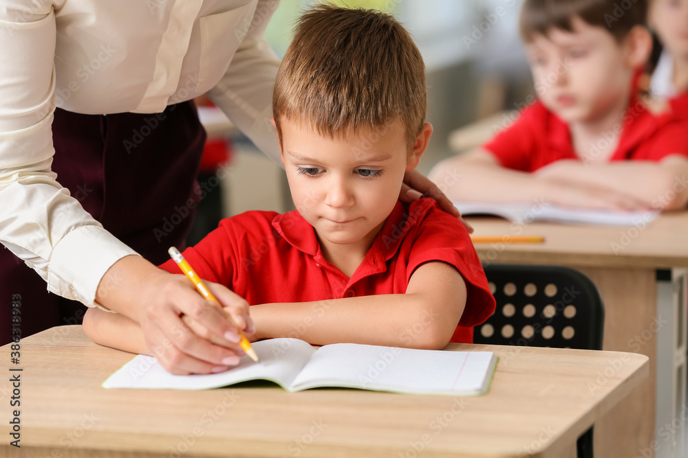 Teacher helping little pupil to write during lesson in classroom