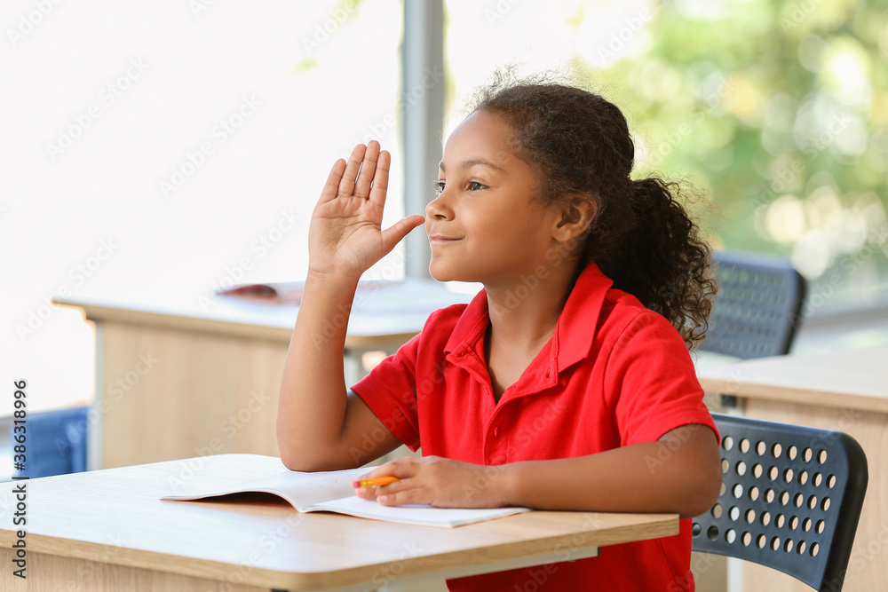 Cute African-American schoolgirl during lesson in classroom