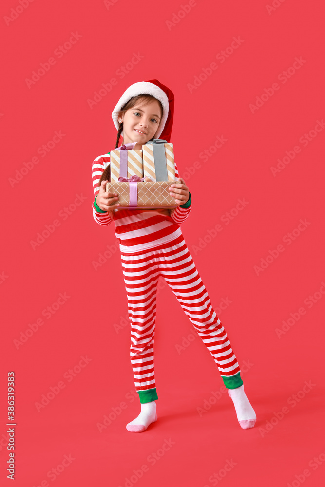 Cute little girl in Santa Claus hat and with Christmas gifts on color background