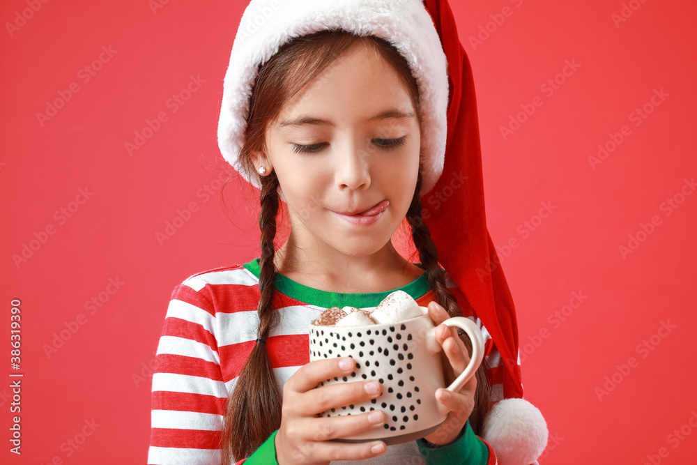 Cute little girl in Santa Claus hat and with cup of hot chocolate on color background