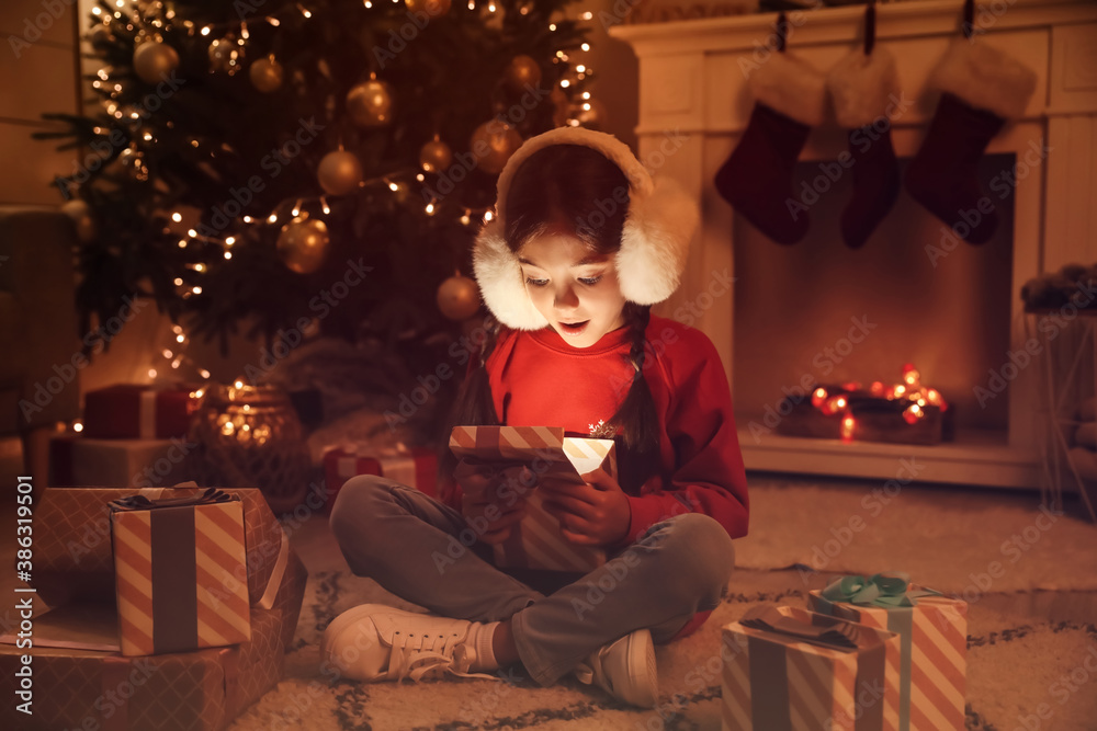 Cute little girl opening Christmas gift at home