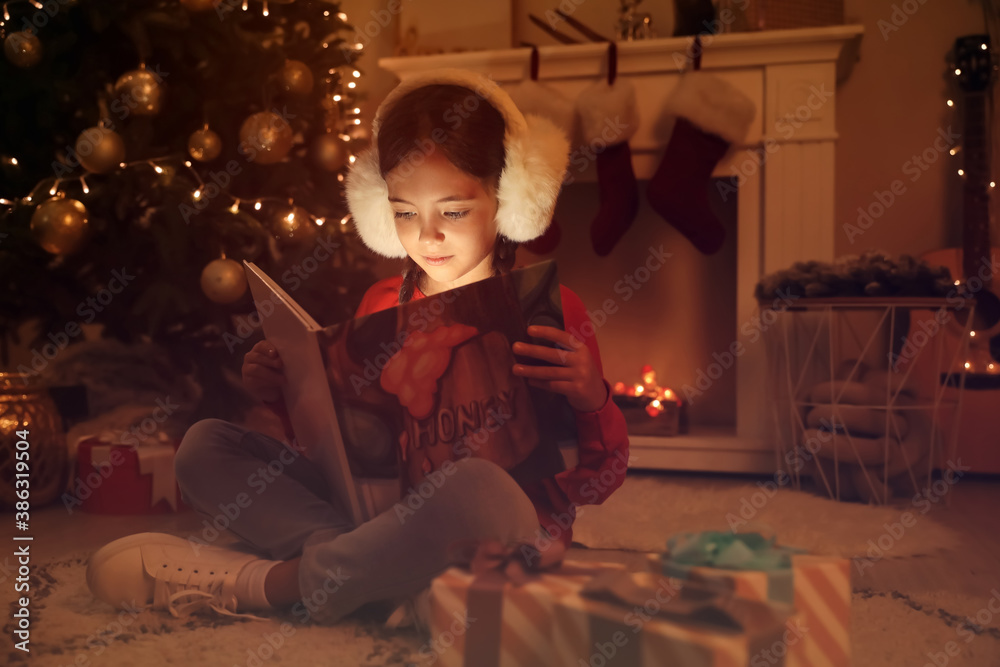 Cute little girl reading book at home on Christmas eve