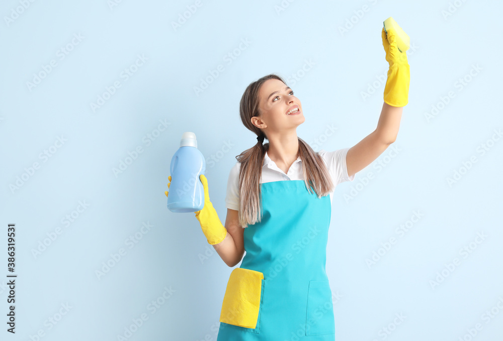 Young woman with cleaning supplies on color background