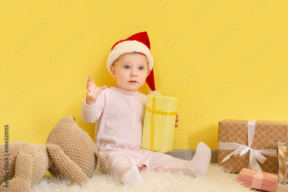 Cute little baby with Christmas gifts near color wall