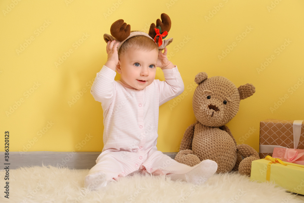 Cute little baby with toy and Christmas gifts near color wall