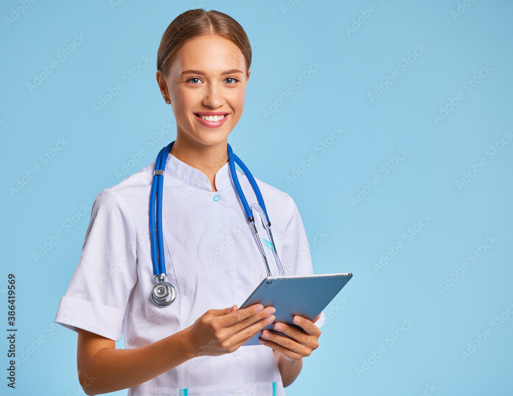 friendly doctor nurse with tablet wireless computer smiles in isolated against ablue background.