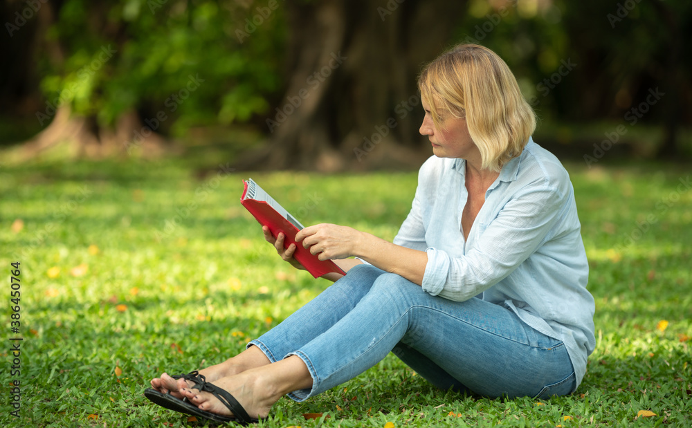 Woman sitting in the grass reading at the weekend. A family reading on the grass.