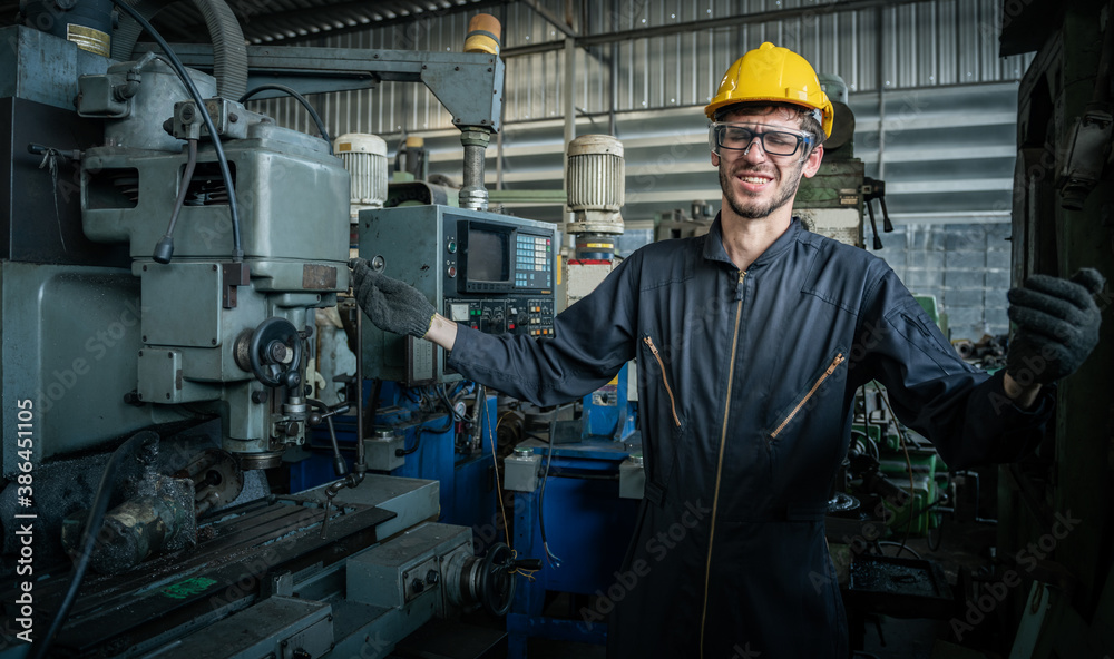 A male engineer is working on an industrial machine. And wear a helmet for safety while working. Con