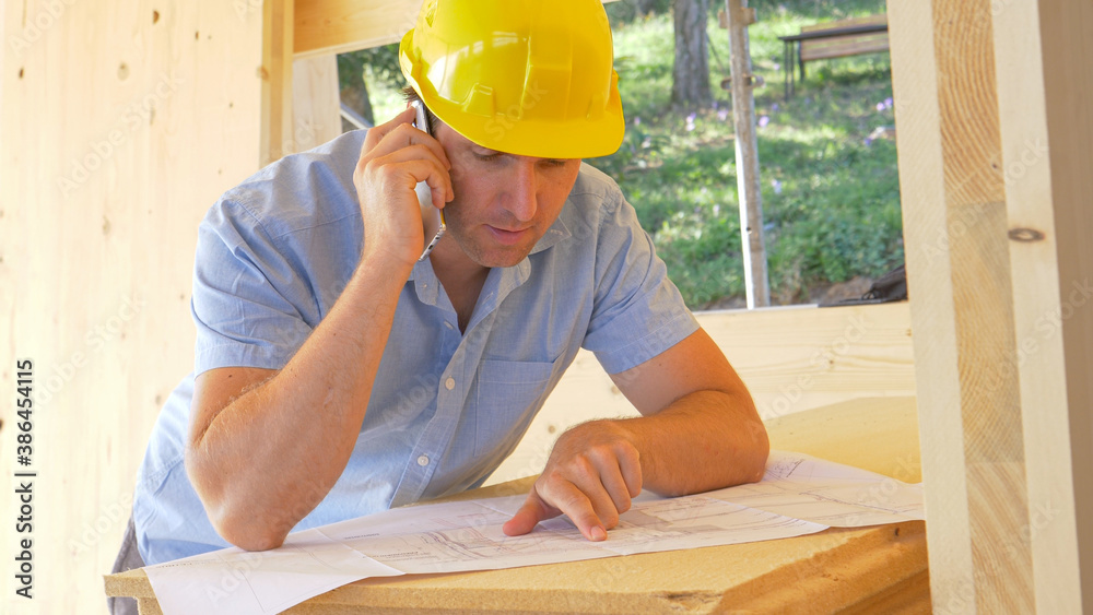 CLOSE UP: Young construction site manager discusses floor plans over the phone.