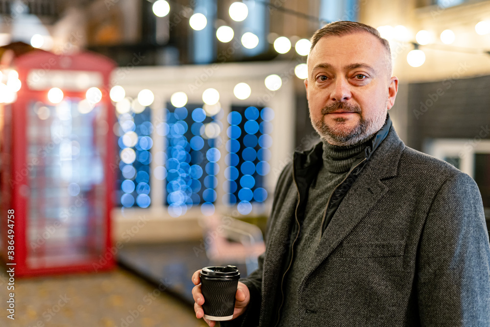 Half length bearded business man in warm clothes holding coffee in hands. Businessman in coat lookin