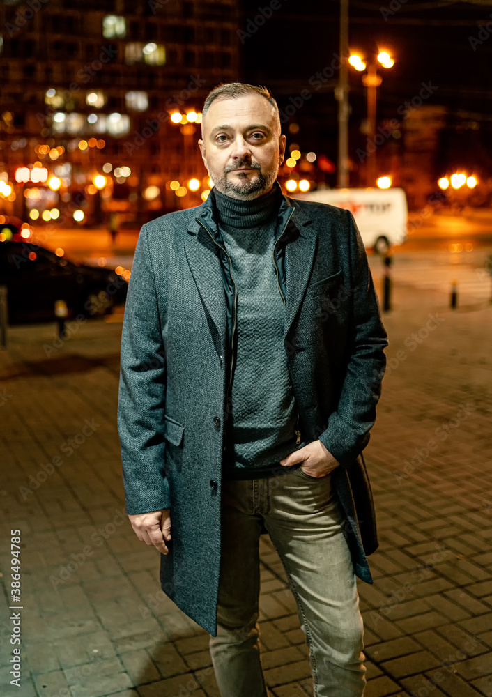 Mature man in elegant coat looking at camera standing in the street. fashion portrait.