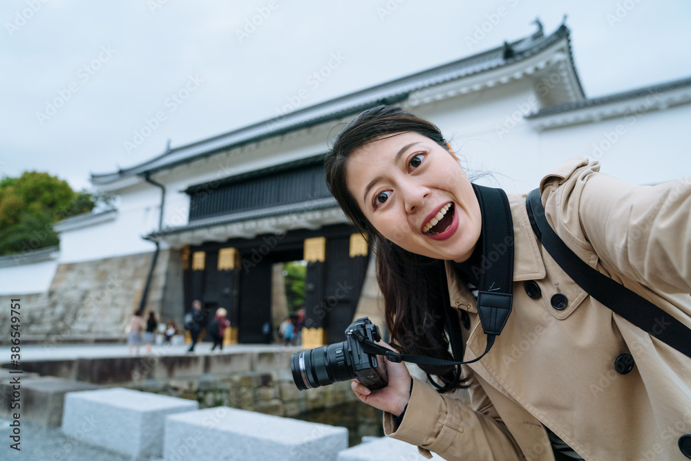 幸福的年轻女士拿着相机在二条城堡入口处用智能手机自拍。a