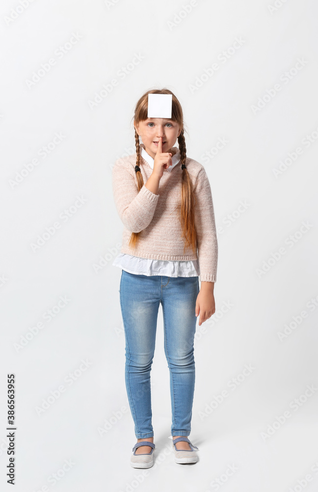 Little girl with blank note paper on her forehead against light background