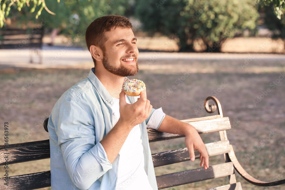 Handsome young man eating sweet donut in park