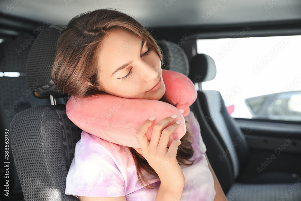 Beautiful young woman with travel pillow sitting in car