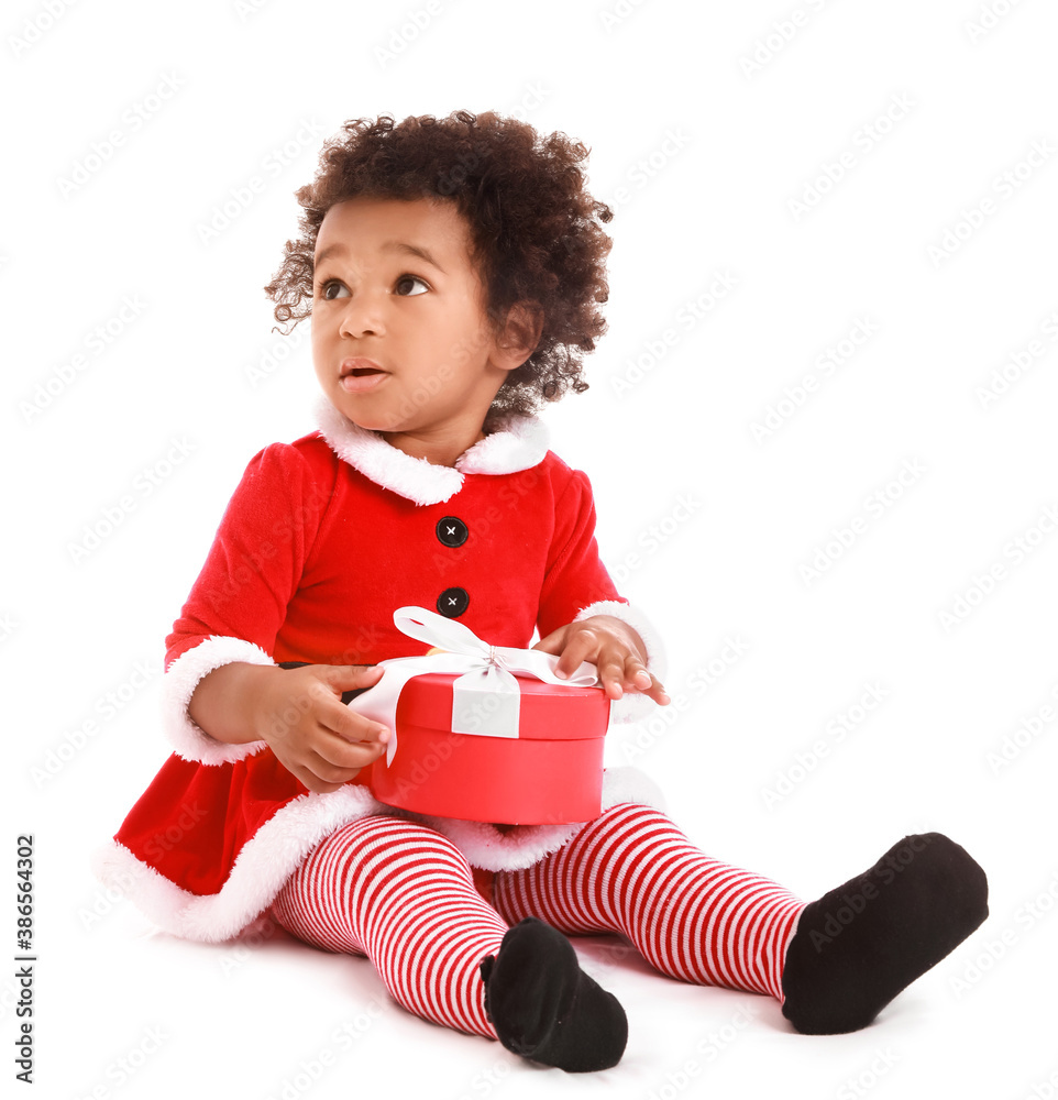 Cute African-American baby girl dressed as Santa and with Christmas gift on white background