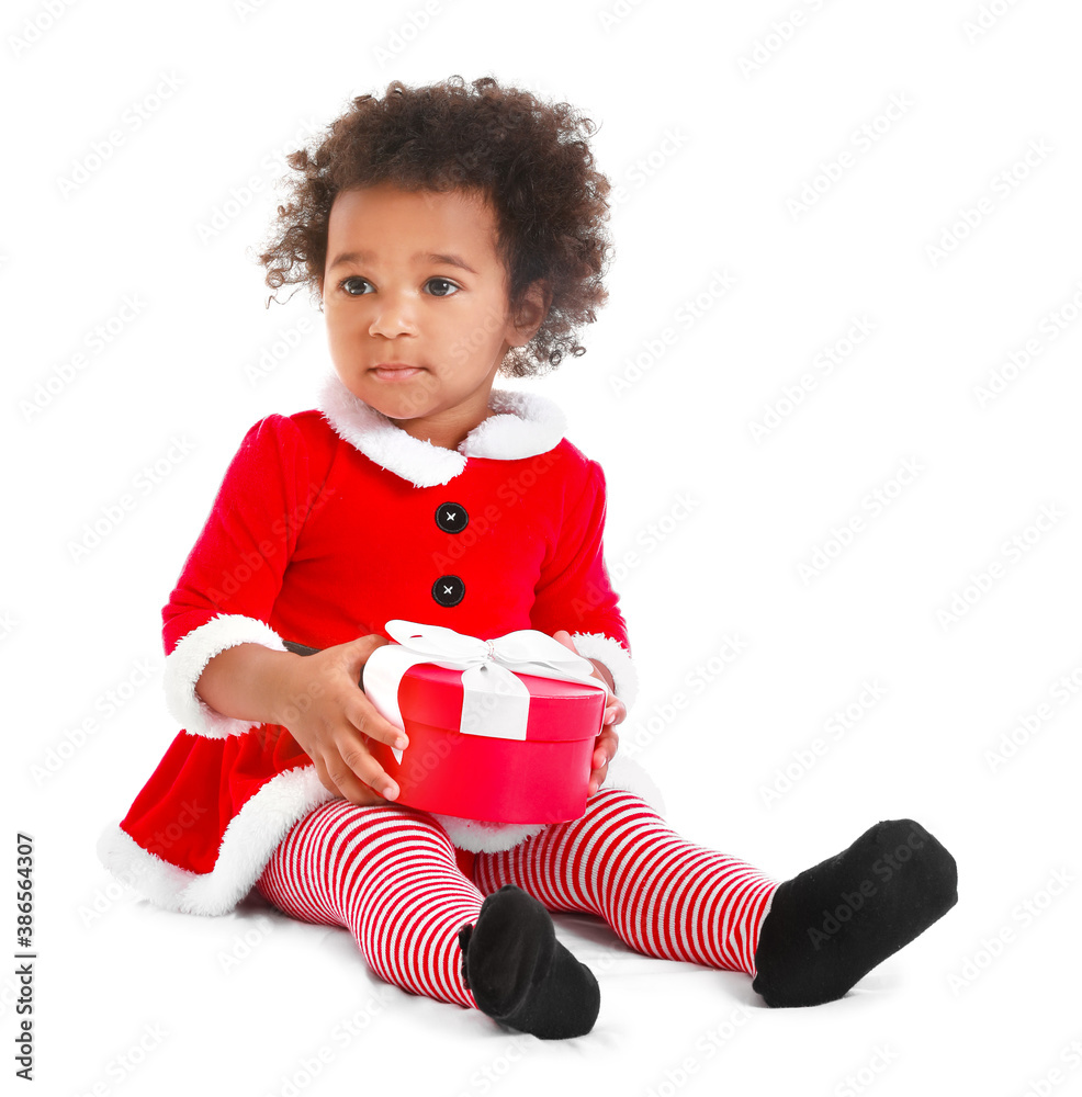 Cute African-American baby girl dressed as Santa and with Christmas gift on white background